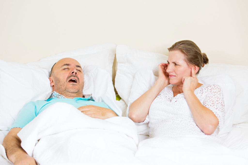 man in bed snoring, annoyed woman plugging ears