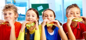 Four schoolkids looking at camera while having lunch during break