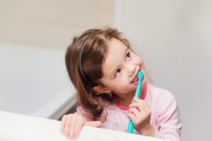 Little girl in pink pajamas in bathroom brushing her teeth