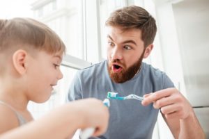 Father and son smiling while brushing teeth in bathroom