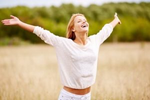 happy woman with outstretched arms standing in field enjoying summer sunshine