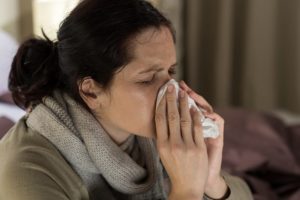 Young sick woman sneezing in tissue sweating from flu fever deciding whether to go to dentist